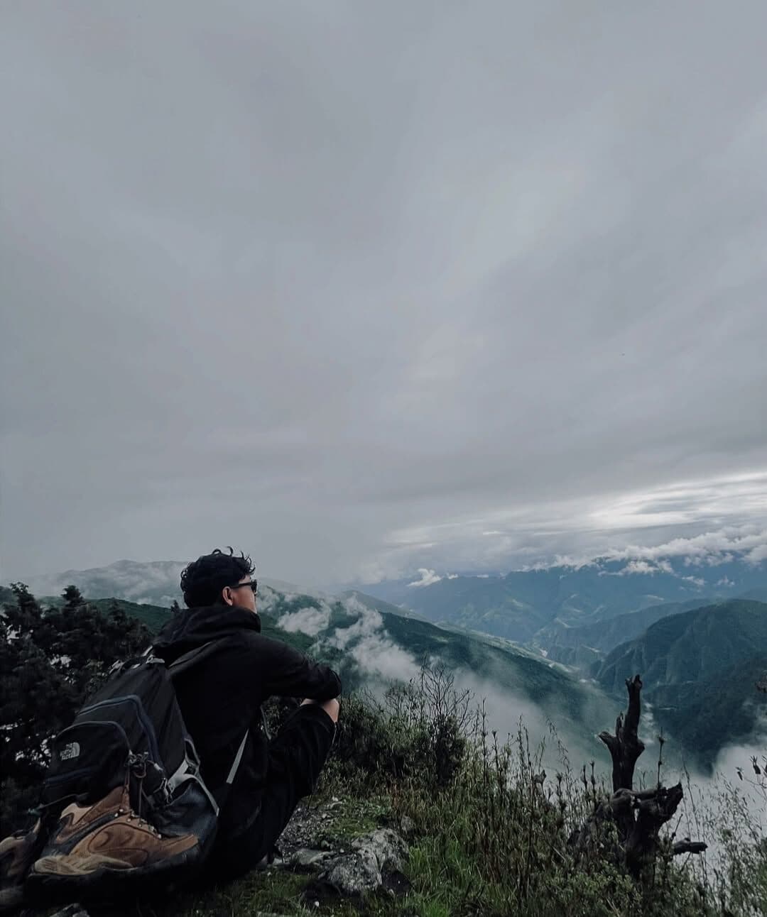 Deepak sitting on a ridge above clouded mountain valleys
