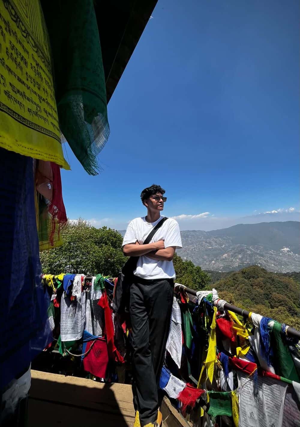 Deepak Bhujel standing by a railing strung with prayer flags under a blue sky