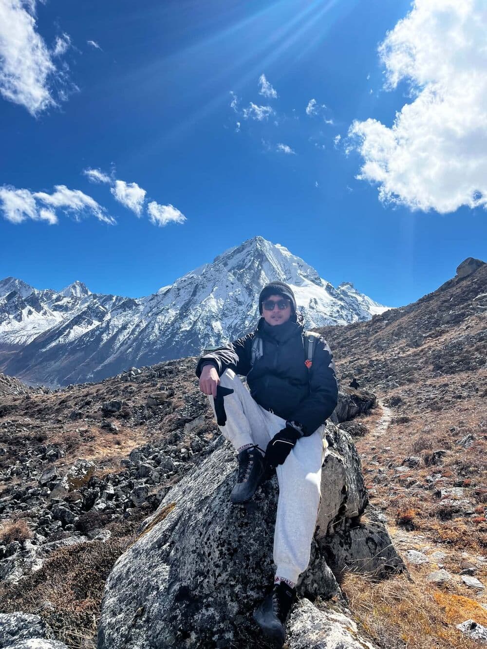 Deepak sitting on a boulder in front of a snow-capped mountain