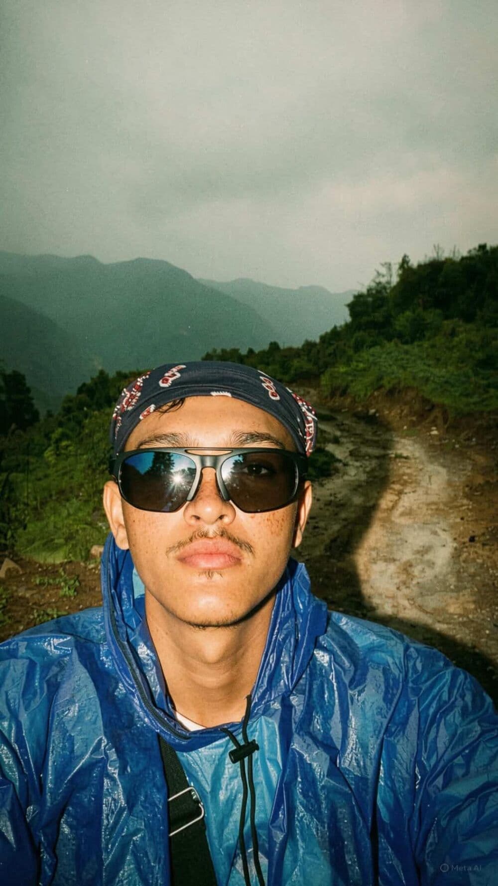 Deepak in a blue raincoat and sunglasses on a misty hillside trail